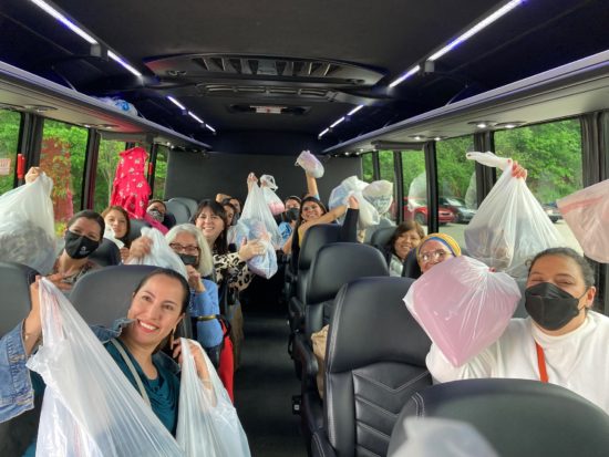 Women on a bus hold up bags full of clothes.