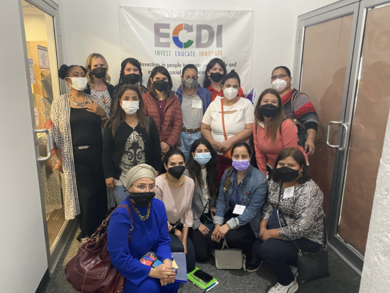 Group of masked women smiling for photo in front of ECDI sign.