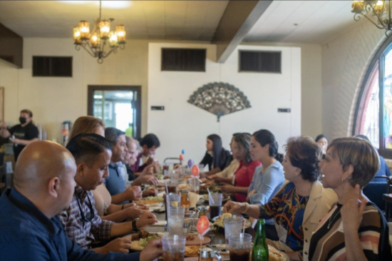 People sitting at long dining table eating a meal and chatting.