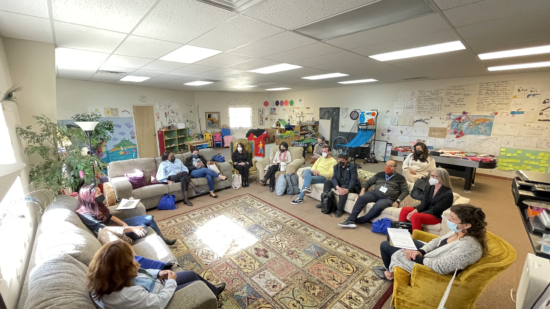 Group of people sitting in a classroom around a rug.