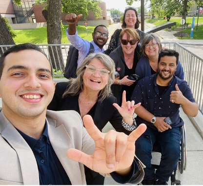 Group of half-dozen poses for selfie outdoors.