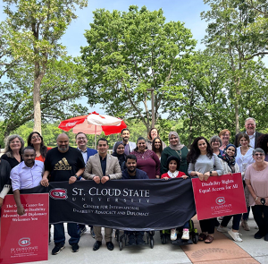 Group of twenty people posing for photo and holding banner outdoors.