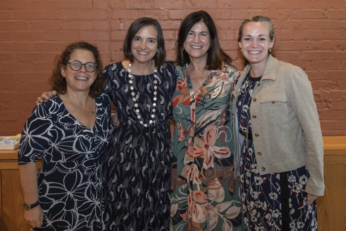 Four women dressed professionally pose for photo in front of brick wall.