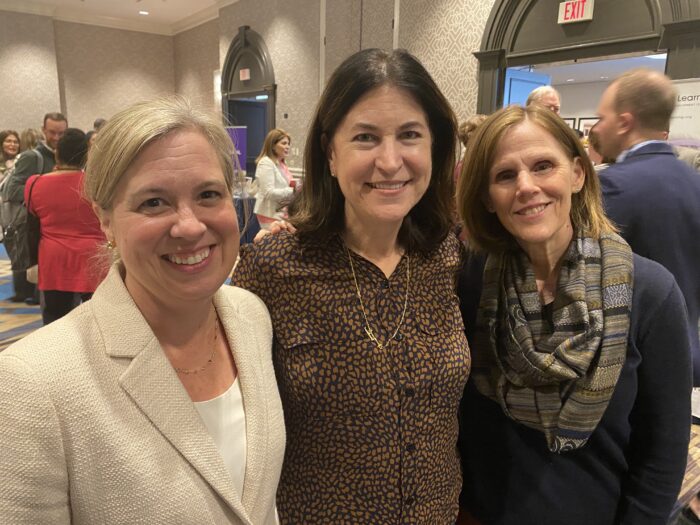 Three women pose for photo during bustling event.