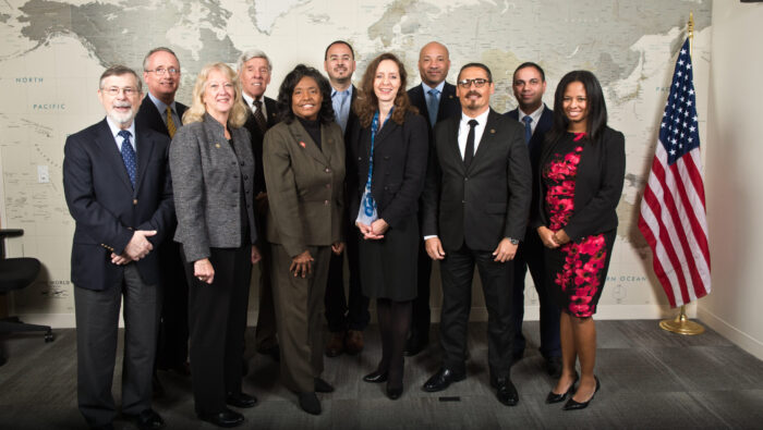 A dozen professionally dressed people pose for picture in front of world map.