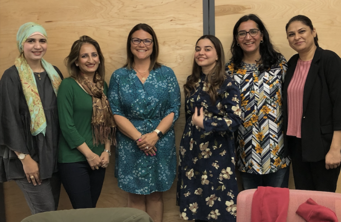 Six women pose for photo in front of wood paneling.