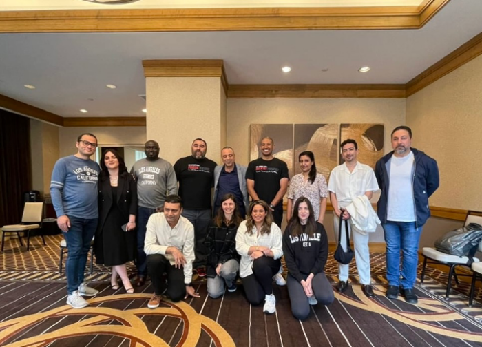 A dozen people dressed casually pose for picture in medium sized room.