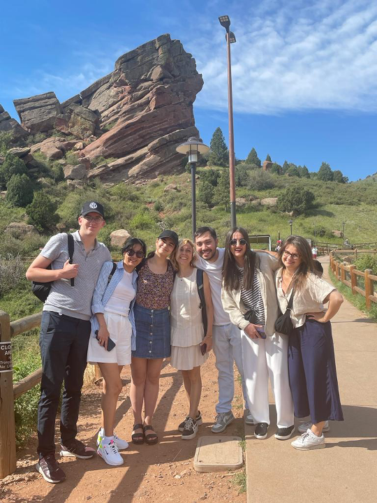 Group of seven young people pose for a picture in front of the hilly Colorado landscape.